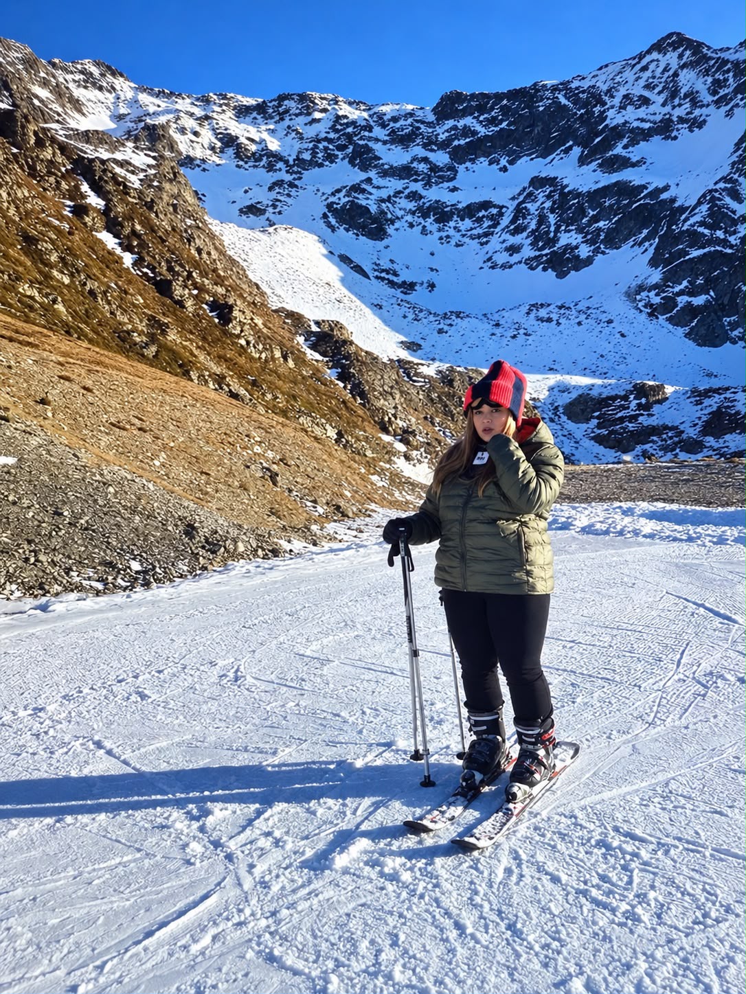 Charlotte aujourd’hui, en tenue de ski sur une piste de montagne, bonnet rouge et noir, doudoune verte
