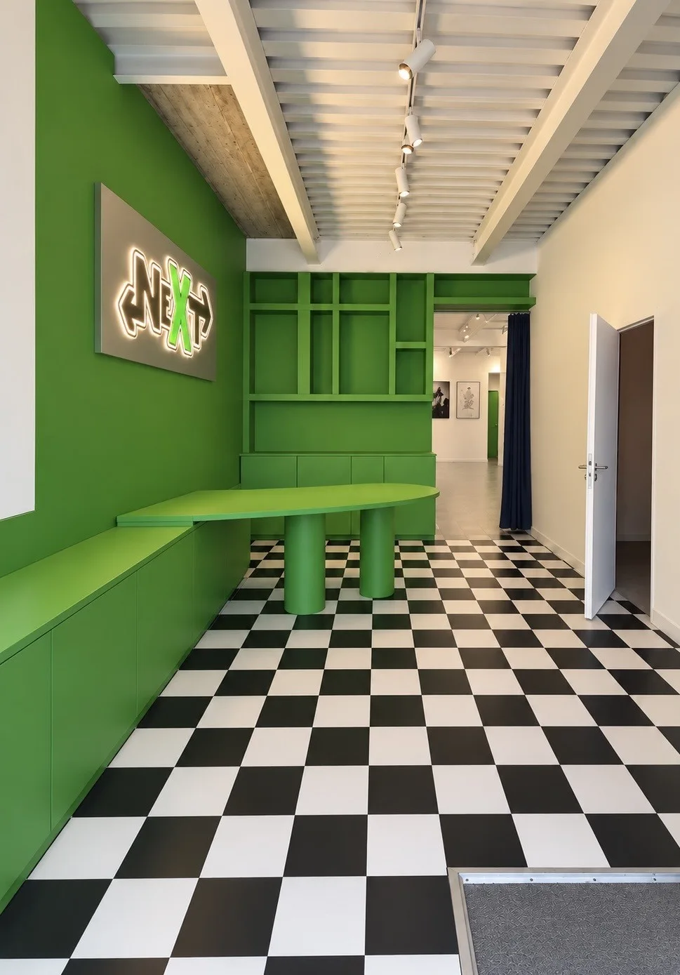 Entrée du club NEXT : mur vert, enseigne lumineuse NEXT et sol en damier noir et blanc